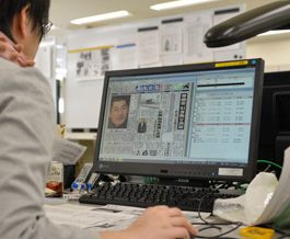 新聞共有システムの組版システムの画面にて紙面制作を行っている整理部員